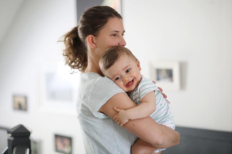 Mother hugging happy baby indoors